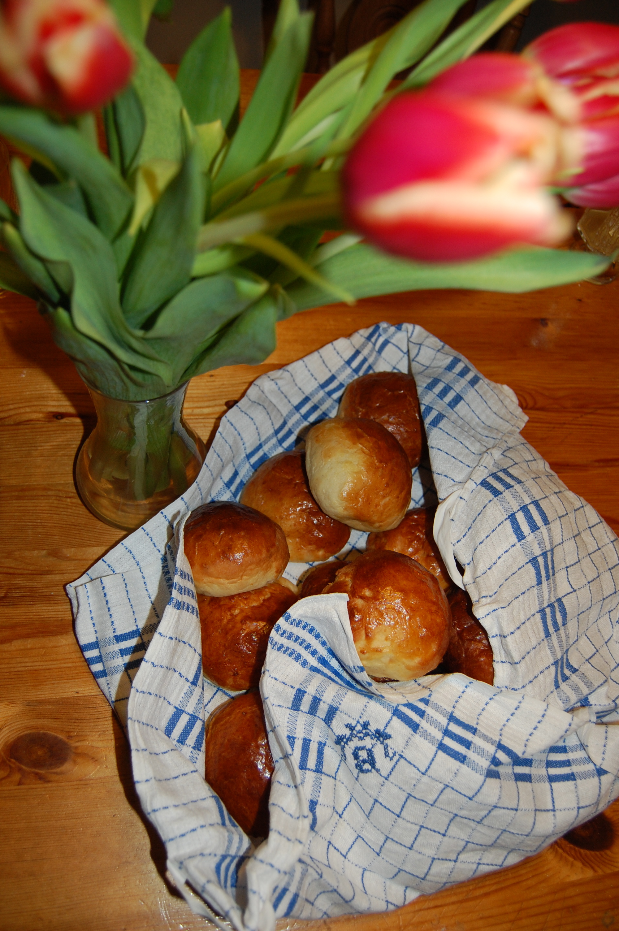 Semmelbullar i en handduk intill en vas med tulpaner